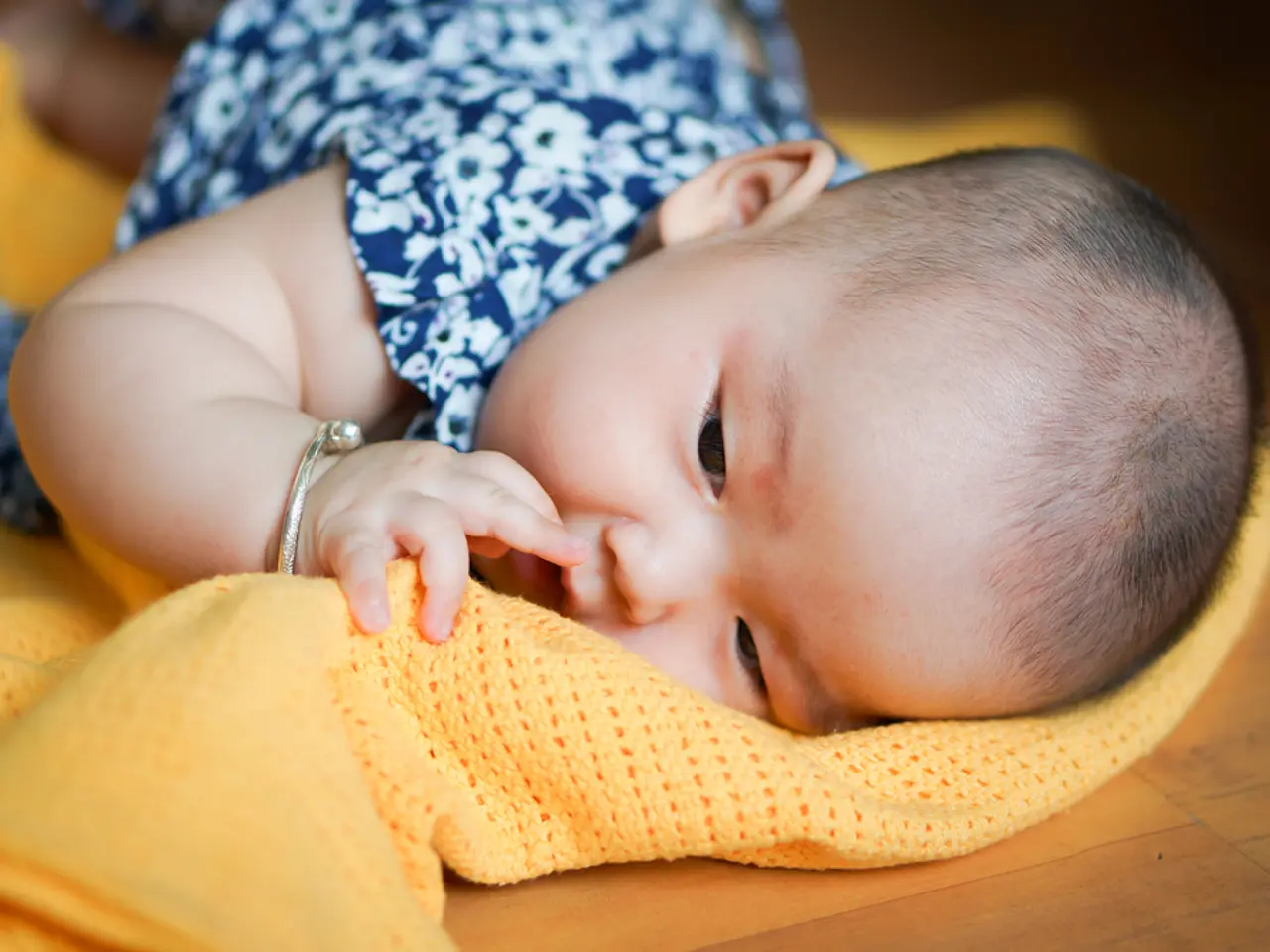 A baby wearing bangle is lying on a cloth and it is on another surface.