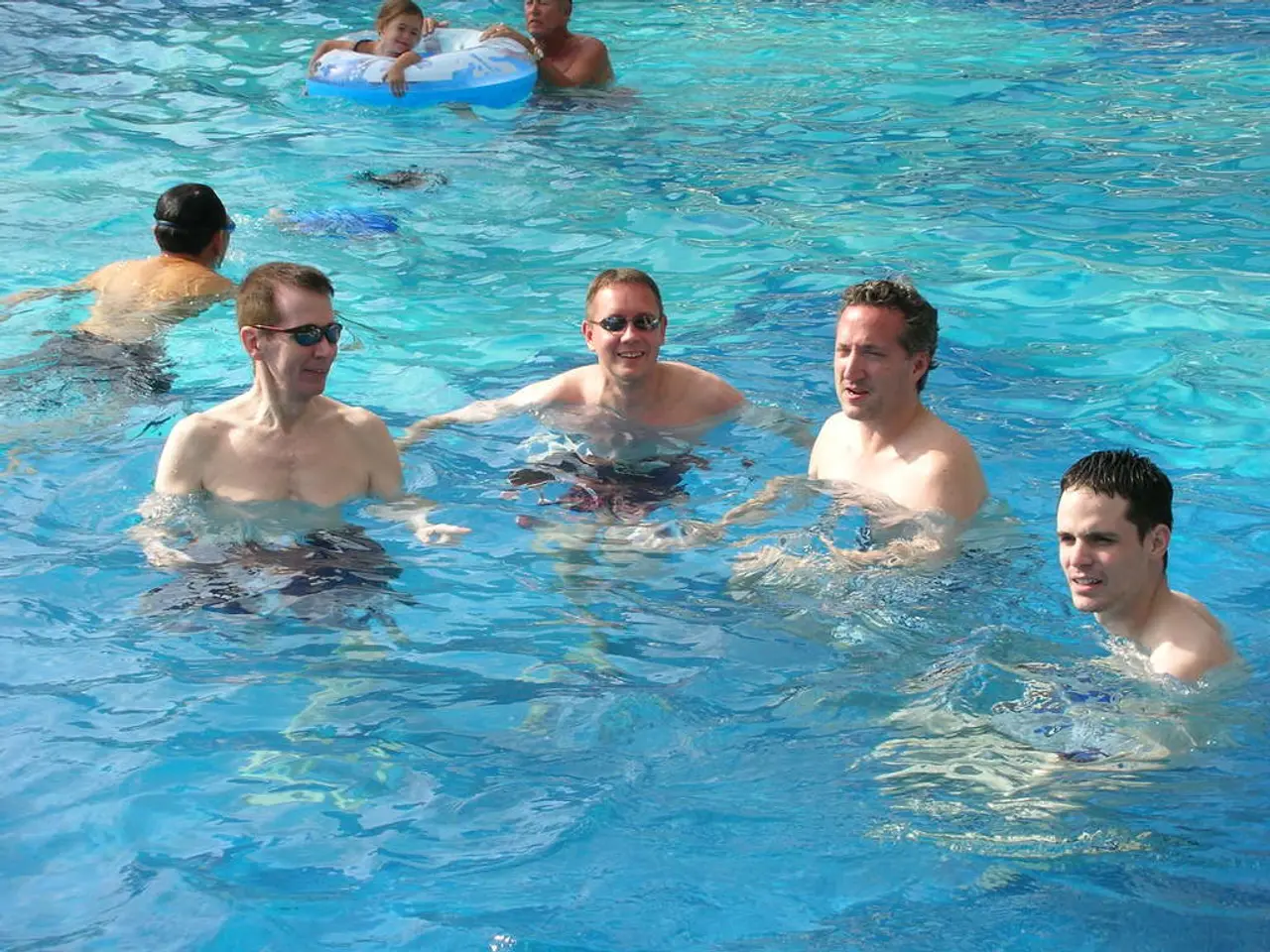 In this image I can see few men swimming in the water. At the top there is a girl swimming by using...