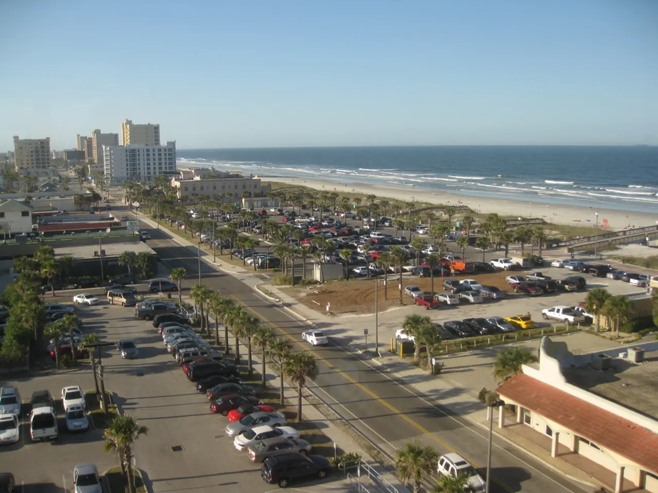 In this image there are vehicles and there are trees, buildings, and there is an ocean.