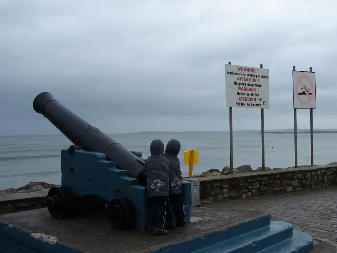 Here we can see military weapon, kids, signboards, rock wall and poles. Background we can see the...