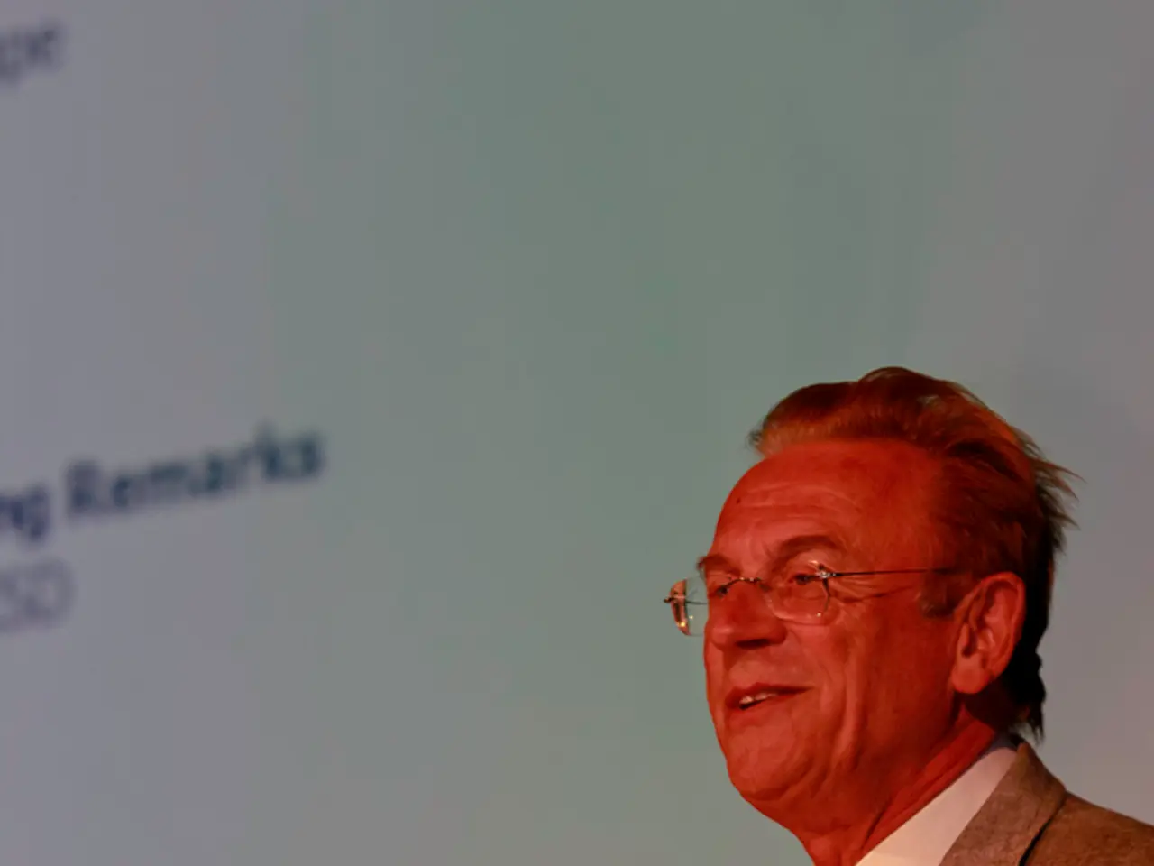 In this picture, we see a man in the white shirt and the grey blazer is standing. He is smiling and...