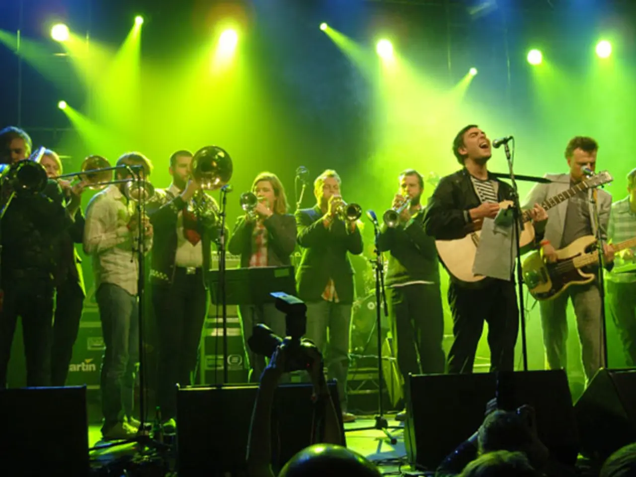 In this image there are many people playing musical instruments. There are mike's. There are...