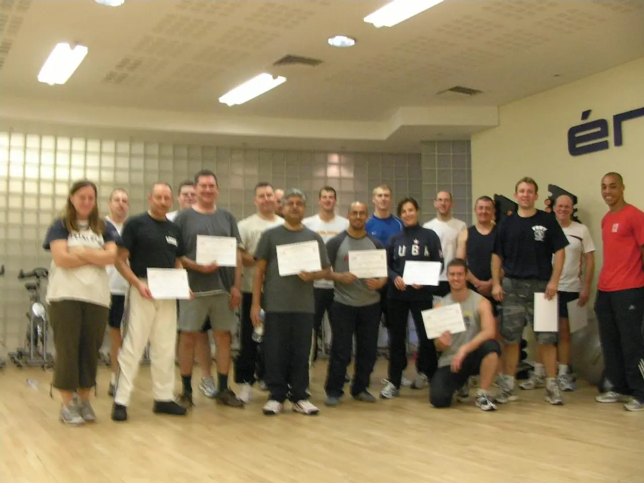 In this image there are group of persons standing and smiling and holding papers. On the left side...