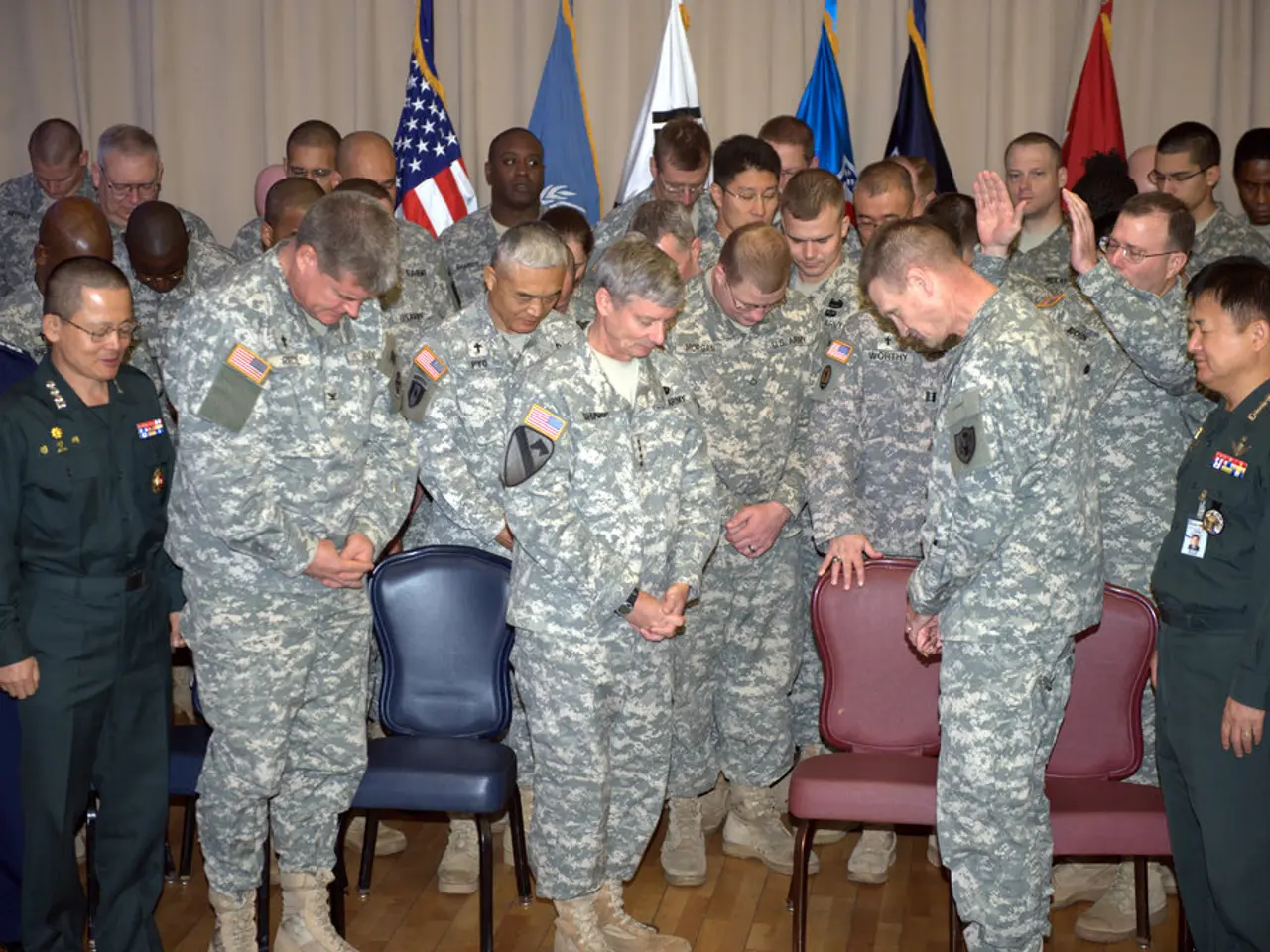 These group of people are standing, in-between of them there are chairs in red and blue color. Most...