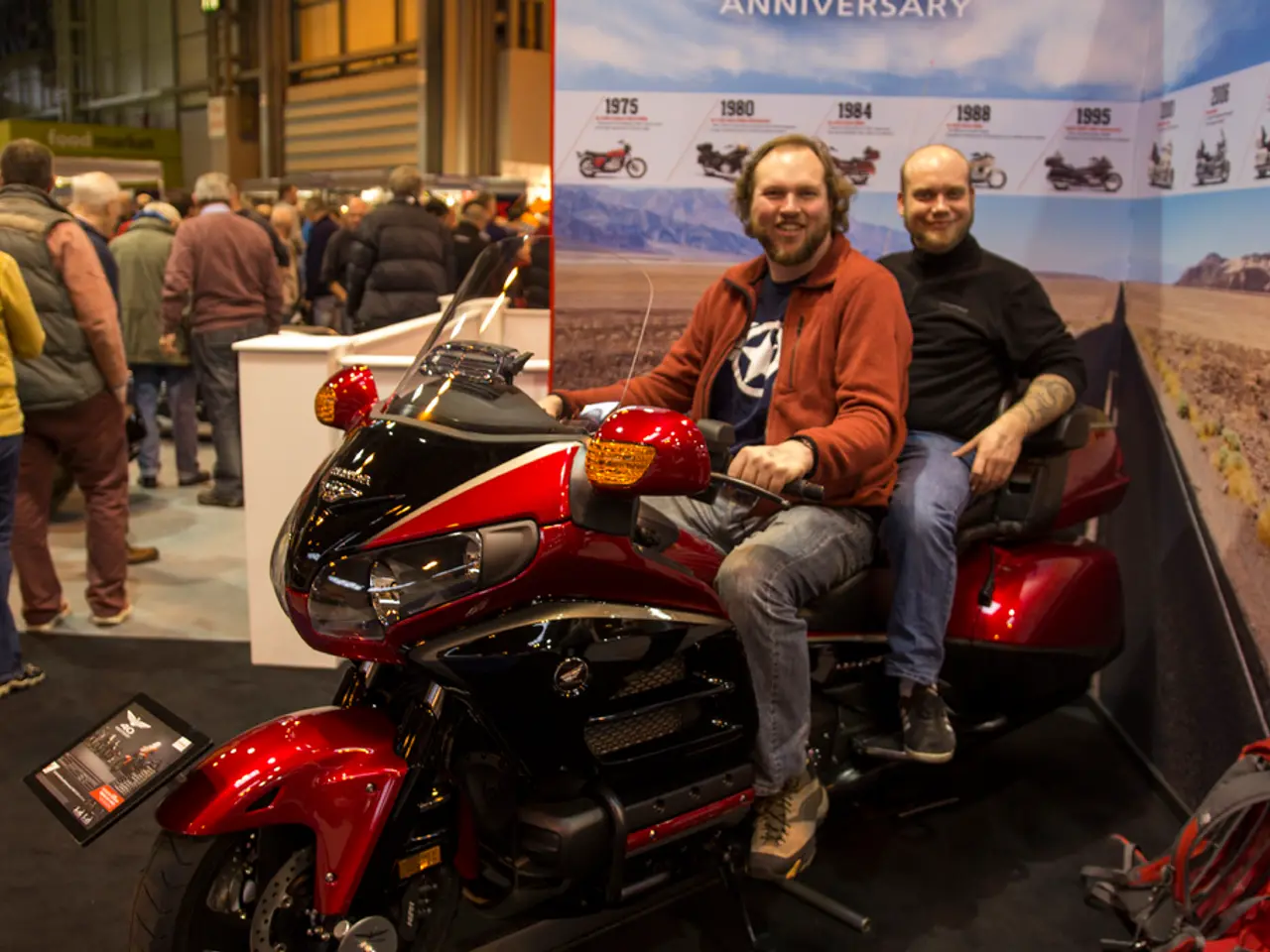 This is the picture of two people who are sitting on the bike and posing and also there are a group...