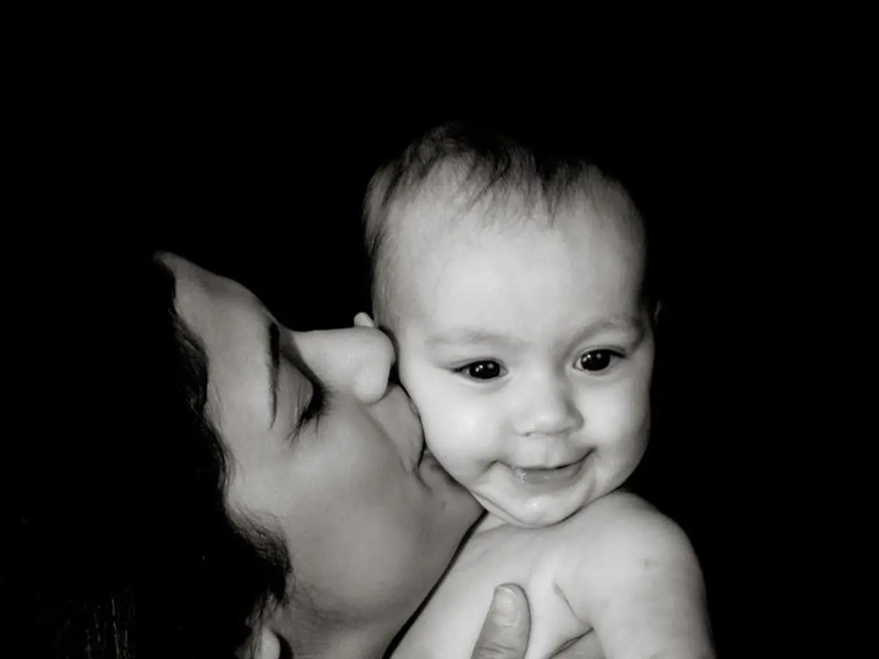 This is a black and white image. In this image we can see a woman holding and kissing the baby.