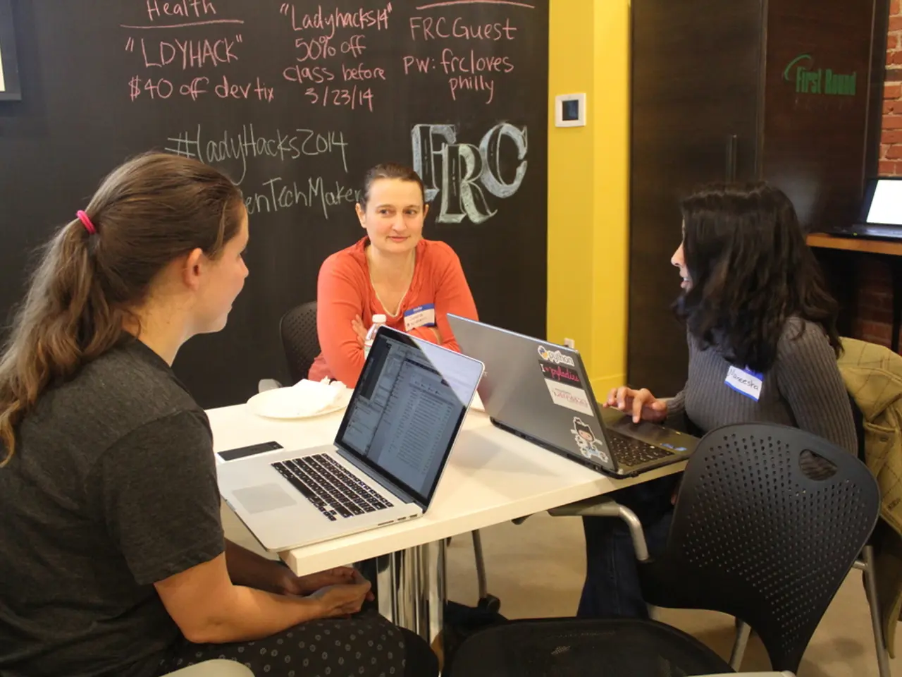 These 3 women are sitting on a chair. On this chair there is a jacket. We can able to see tables,...
