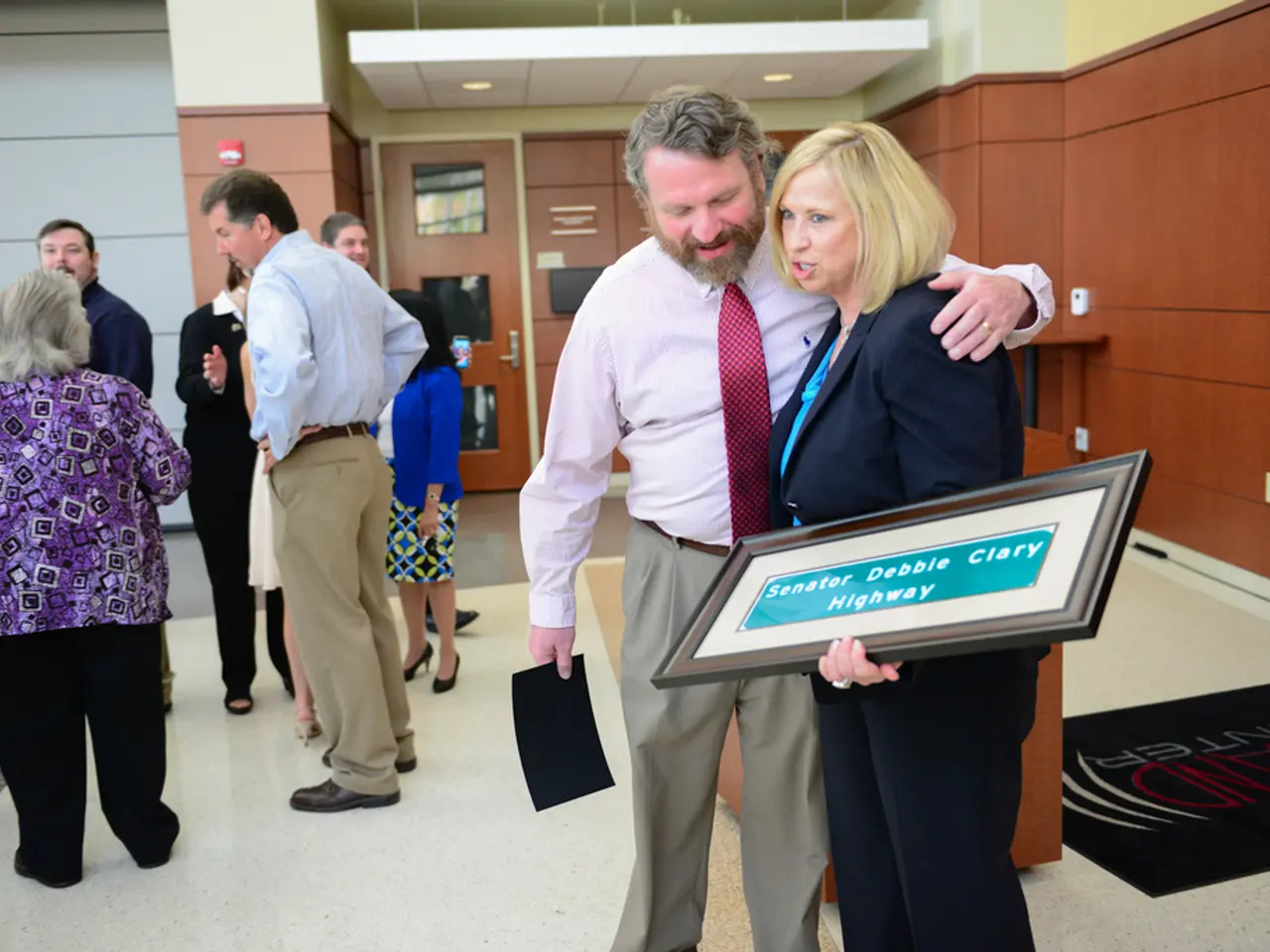 In this image there are group of personś standing, there is a person holding an object, there is a...