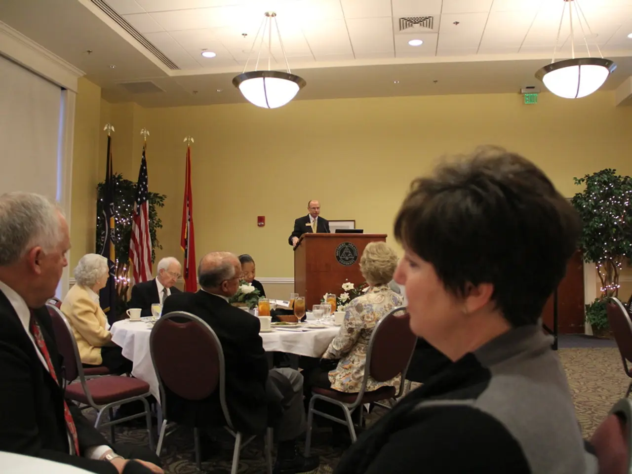 In this image I see few people who are sitting on the chairs and there is a table in front of them...