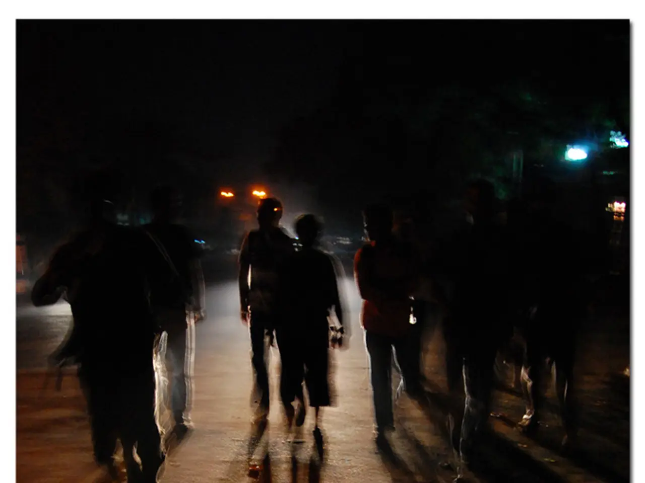 In this picture there are few persons walking on the road and there is a light behind them and...