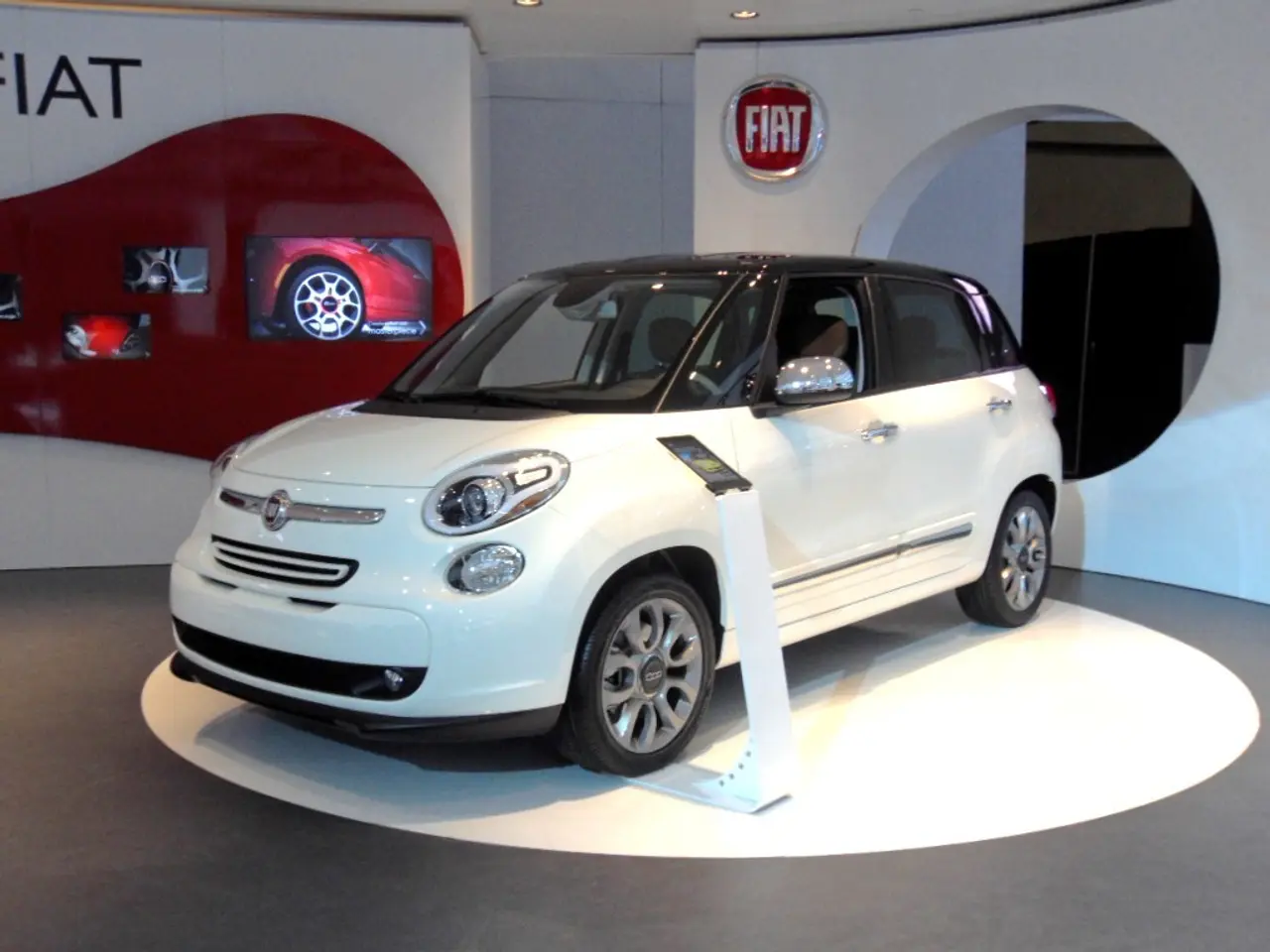 There is a car on the floor. Here we can see screens, board, lights, and wall.