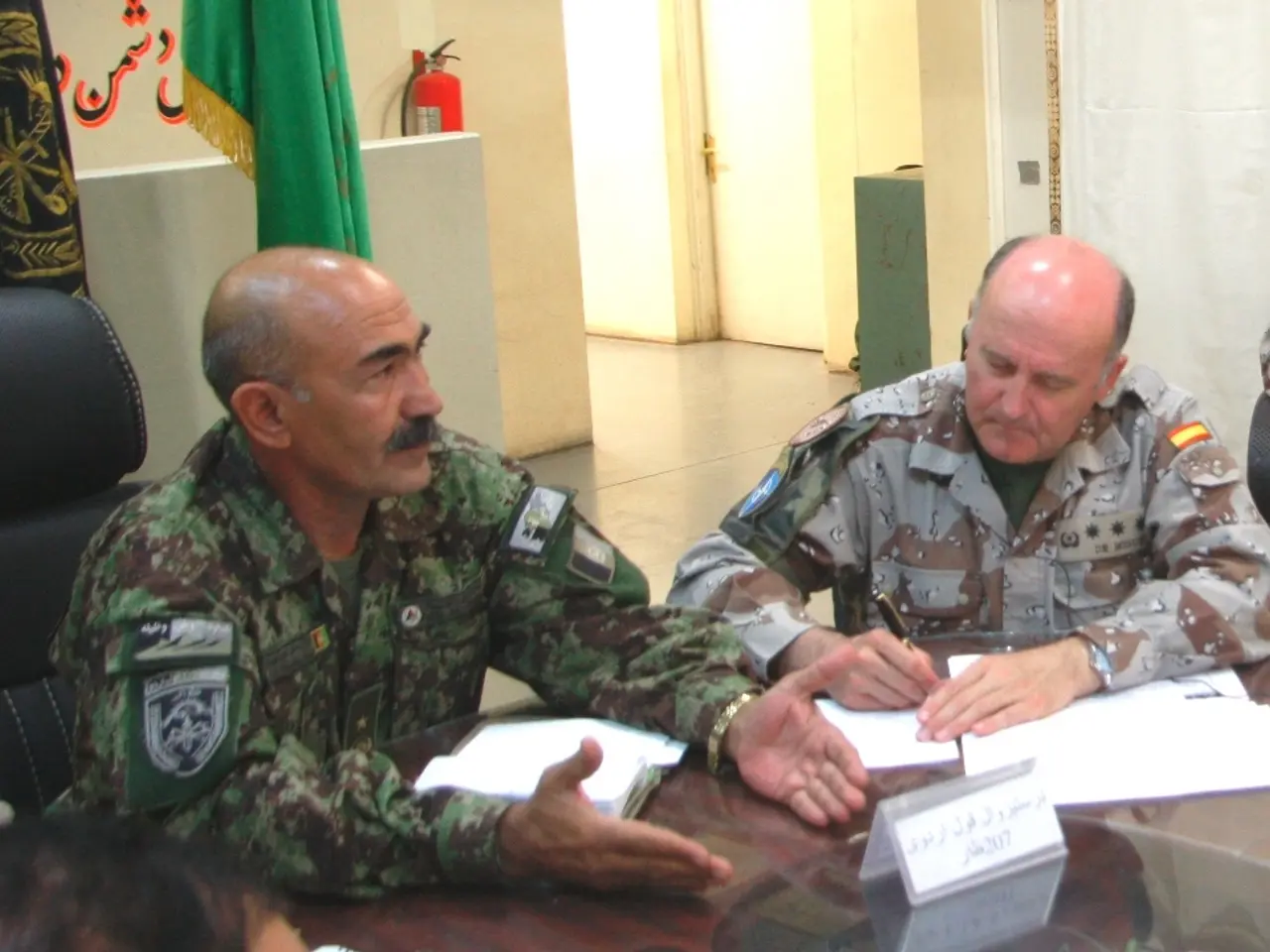 In this image we can see two people are sitting, they are wearing army uniform. In front of them...