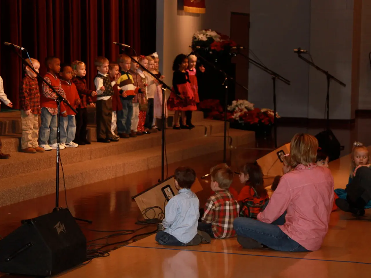 This image consists of many children on the dais. And there are mics along with mic stands. At the...