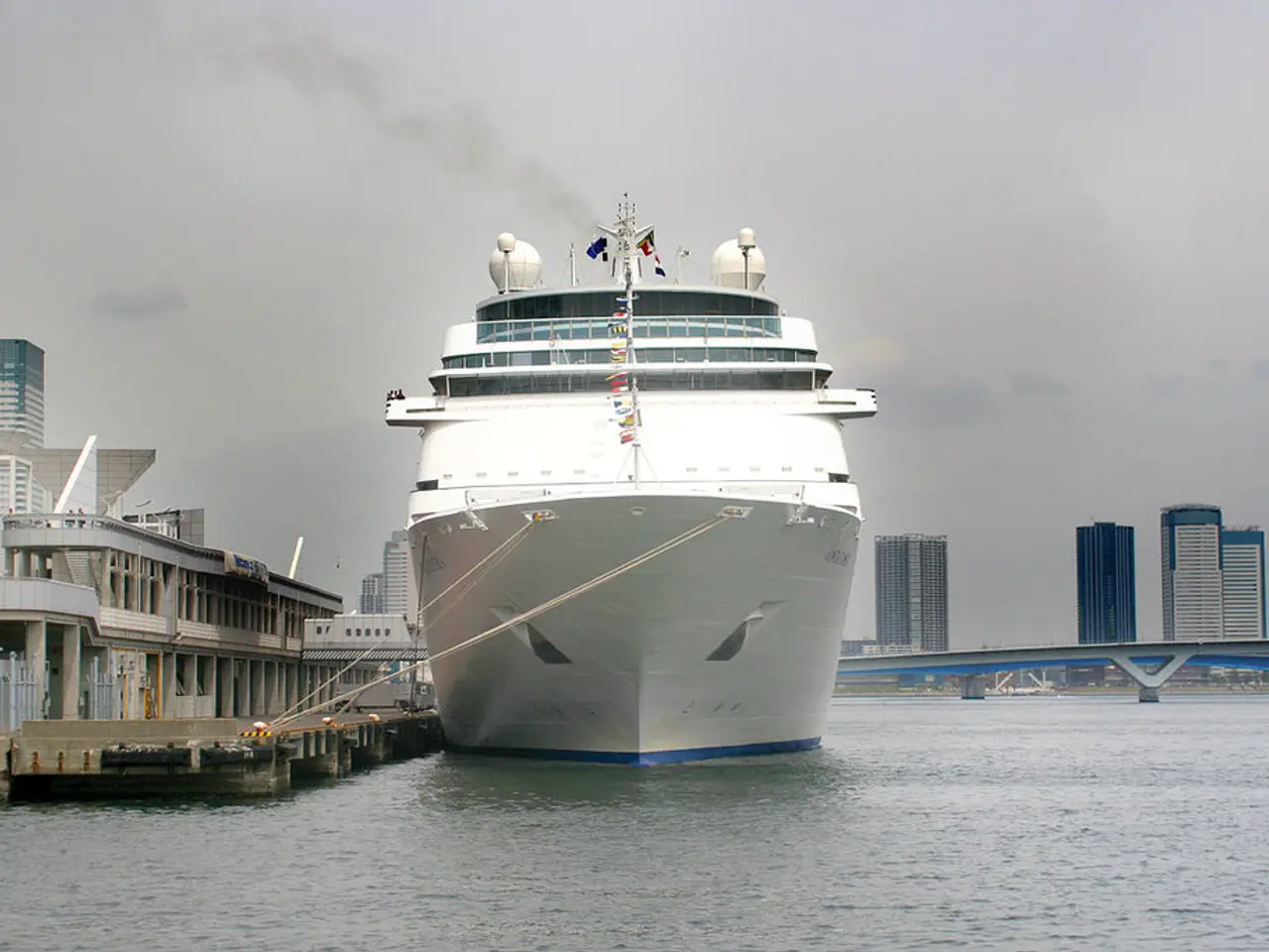 In this image there is a ship floating on the water beside that there is a bridge and so many...
