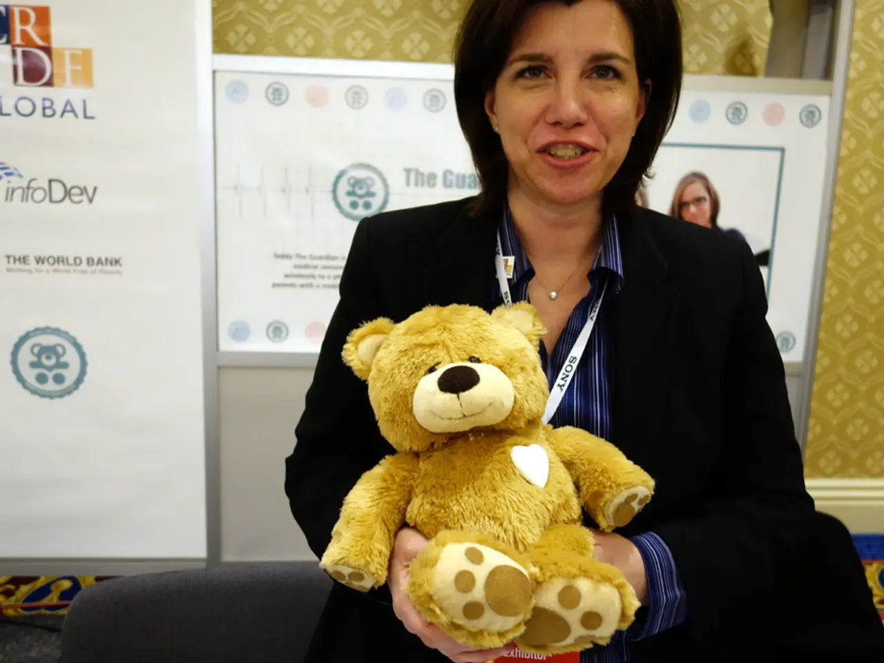 This is the woman standing and smiling. She is holding a teddy bear in her hands. This looks like a...