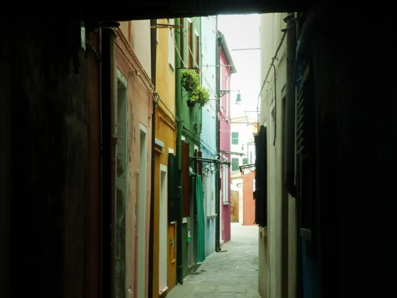 There are buildings on the both side. On the building there are pipes, pot with plants. In the back...