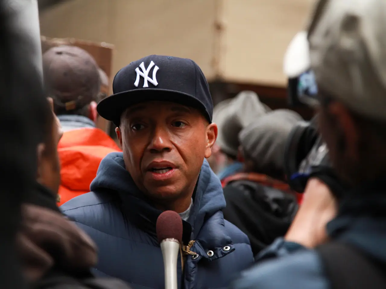 In this image there is a person wearing blue jacket is behind a mike. Behind him there are few...