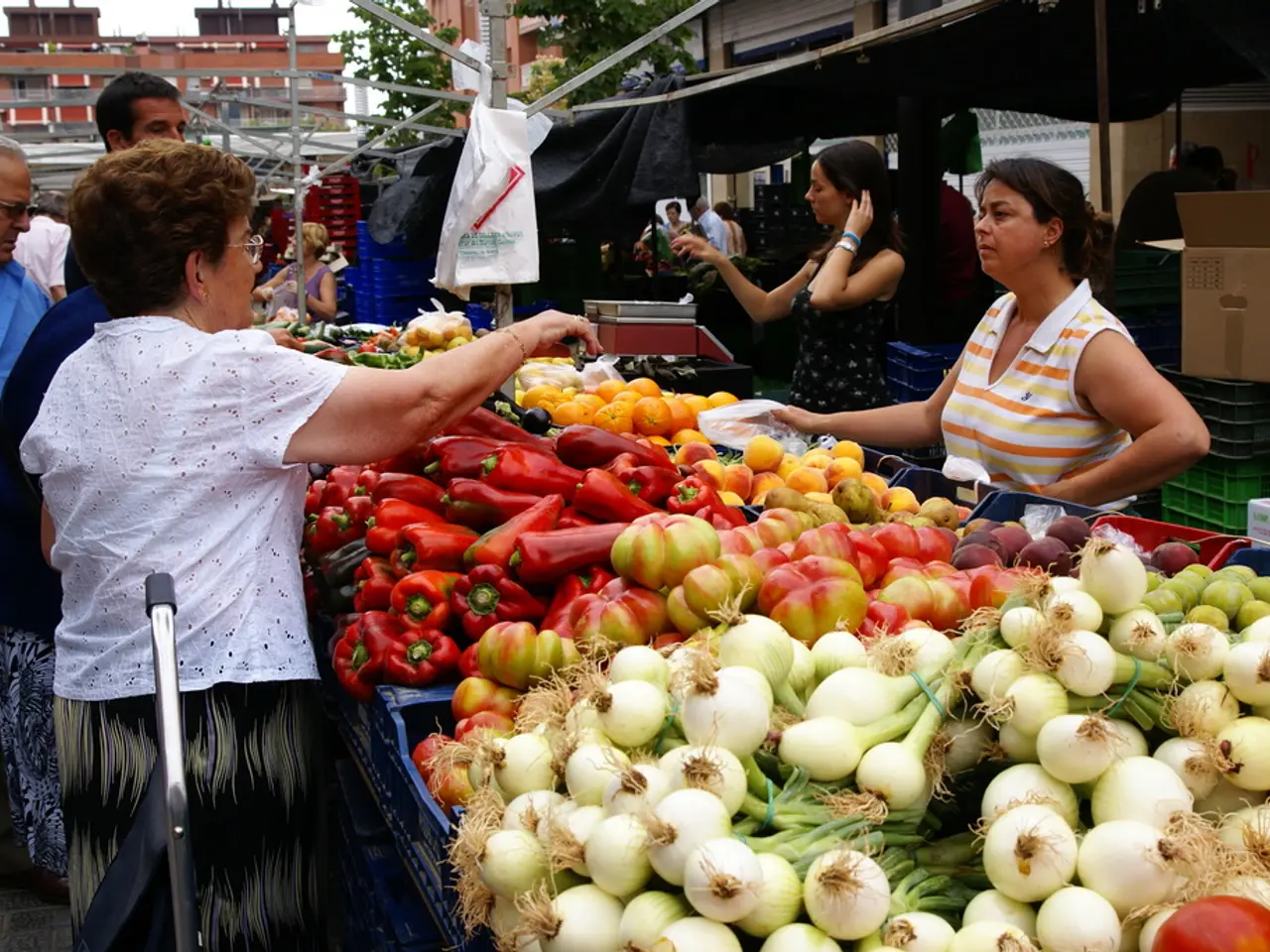 In this image there are vegetables in plastic containers, group of people standing, buildings,...