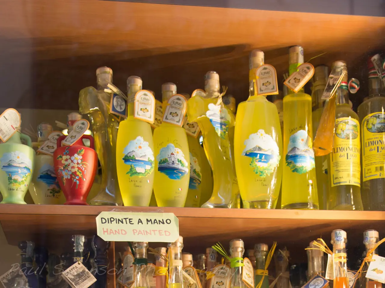 It the picture there are lot of bottles placed in the shelf and also some arts , painting arts...