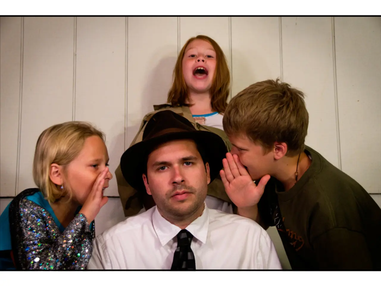 In this picture, we see the man in white shirt and a black hat is sitting. He is looking at the...