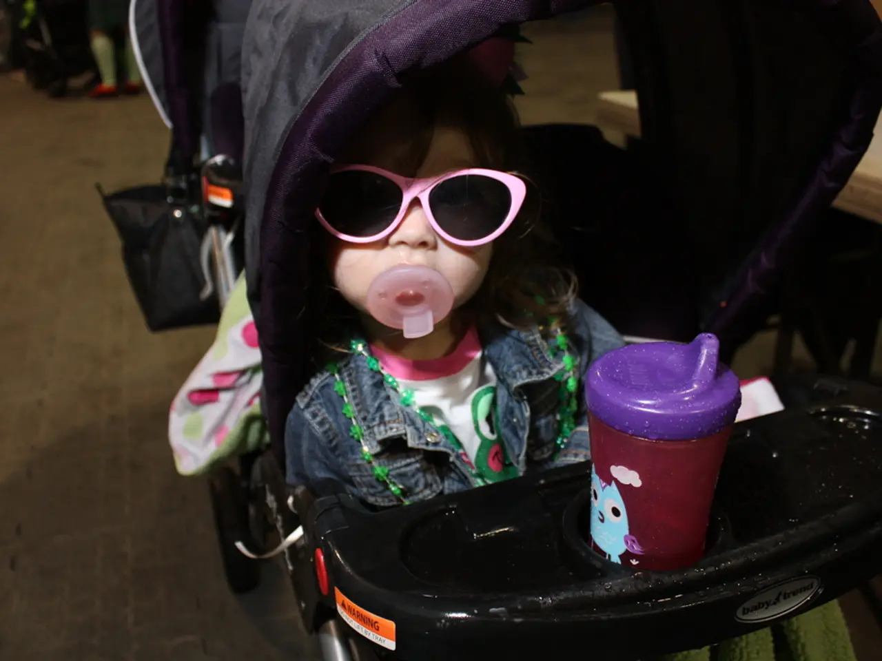 In this image we can see there is a kid sitting in a walker, which is on the road.