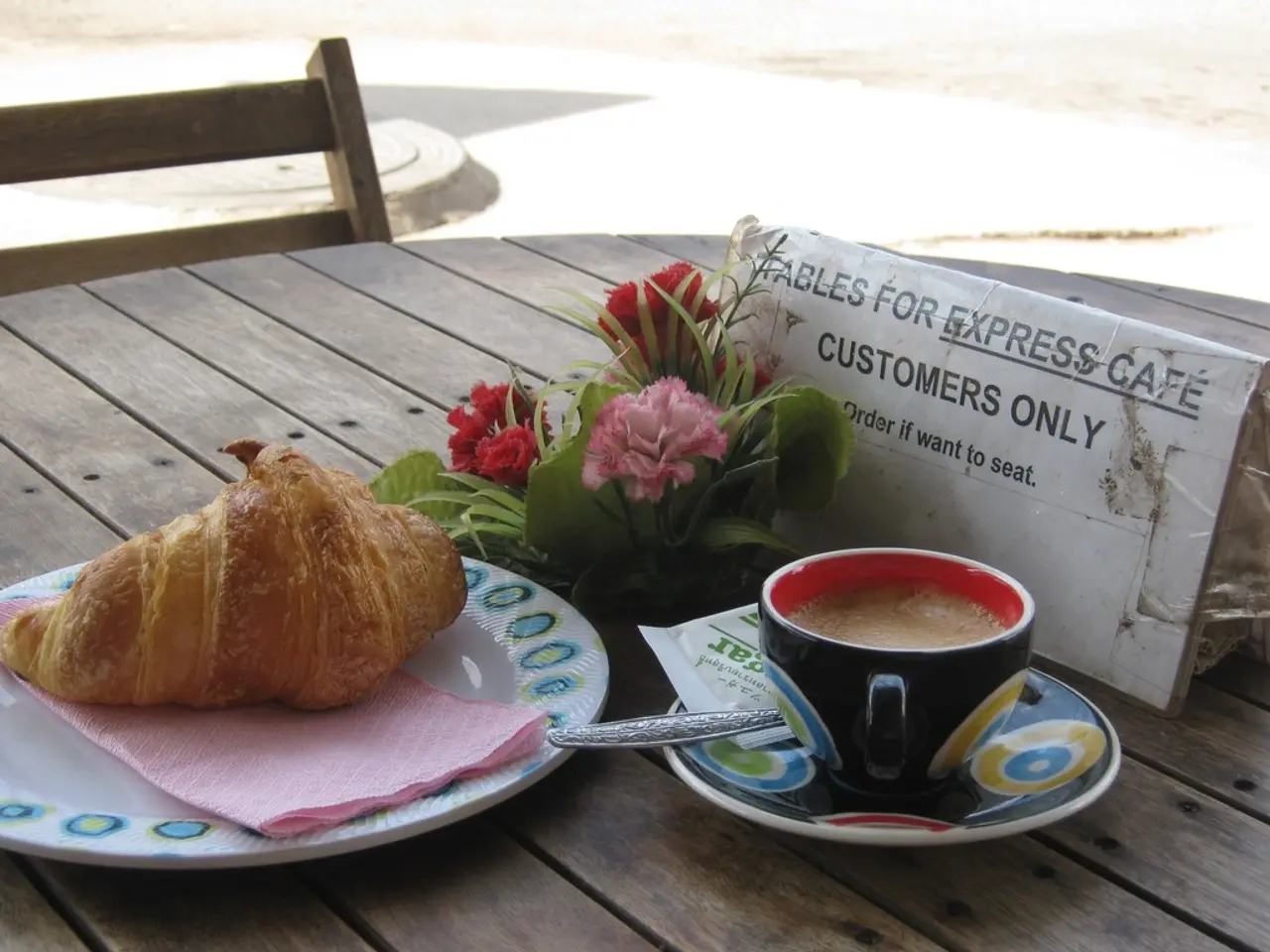 There is a cup of tea on a saucer, spoon, puff pastry on a plate, spoon, flowers, tissue and a...