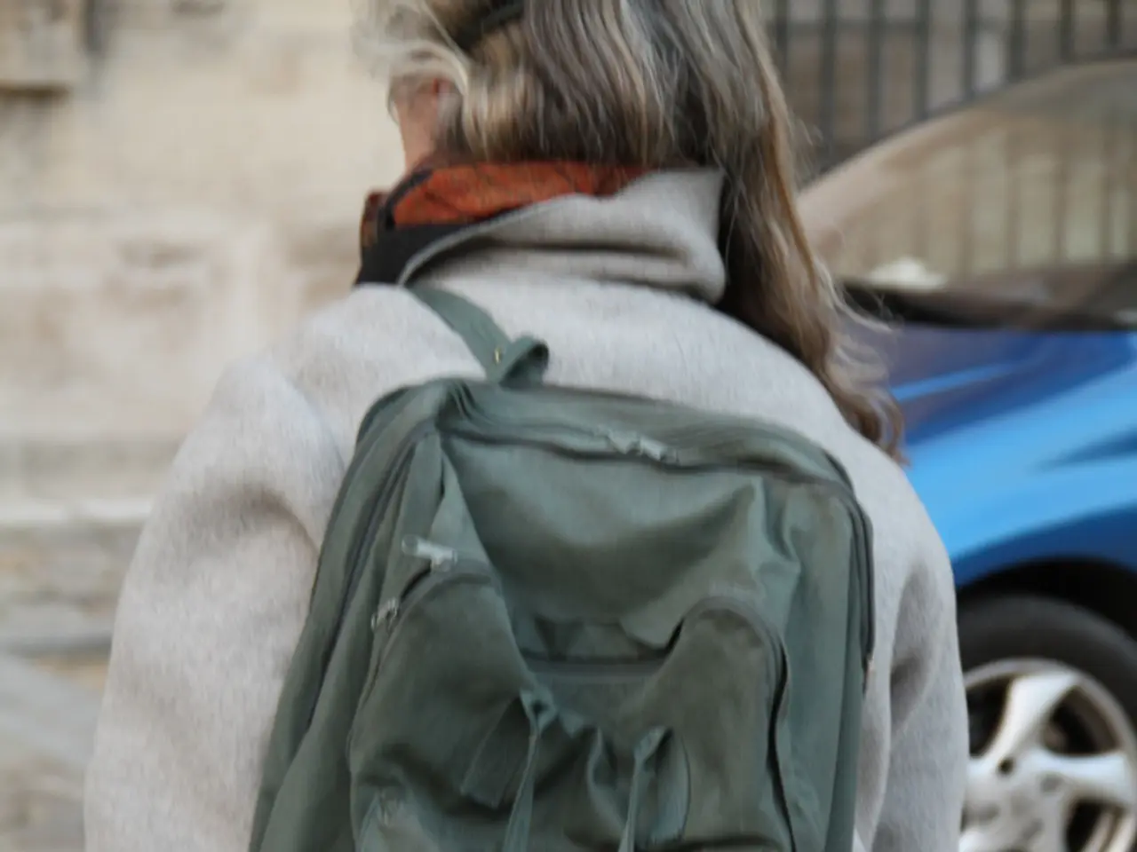 As we can see in the image, there is a woman wearing bag and on road there is a car.