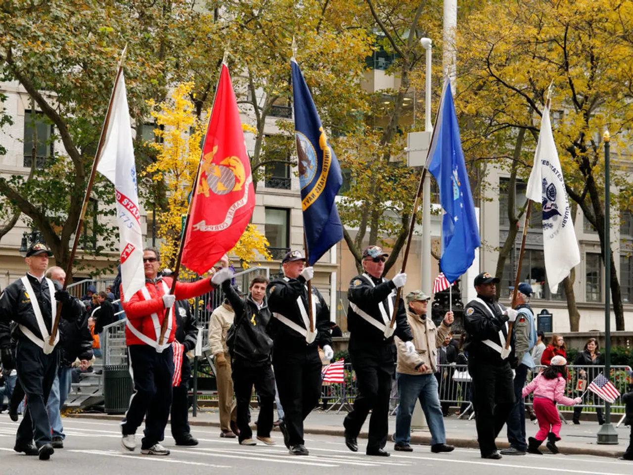 In the center of the image we can see people holding flags. On the right there is a pole. In the...