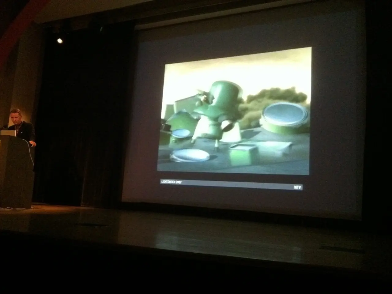 To the left side of the image there is a person standing near a podium. In the background of the...