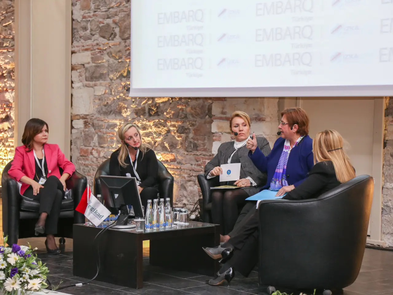 This picture shows few woman seated on the chairs and holding some papers in their hands and they...