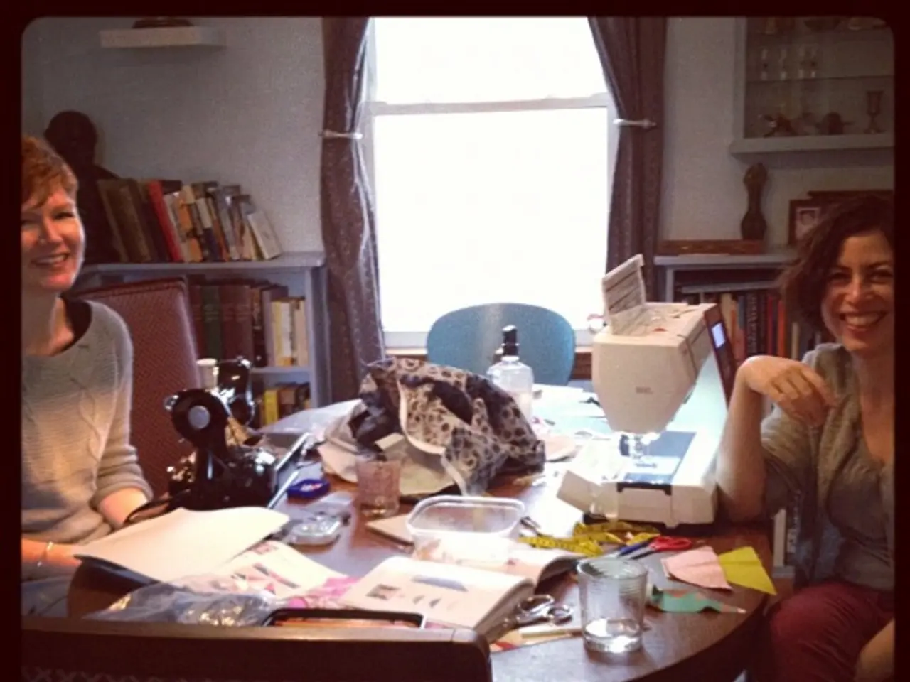 this picture shows two women seated on the chairs and we see glass, papers and a sewing machine on...