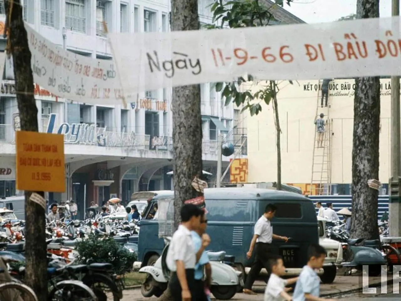 At the bottom of the image there are people, bikes, van and cars. In the background there are...