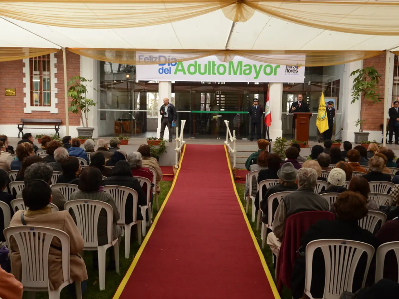 In the image we can see there are lot of people who are sitting on chairs and in front there is a...