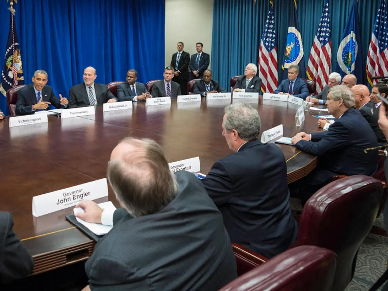 There are group of people sitting in chairs and there is a table in front of them and there are few...