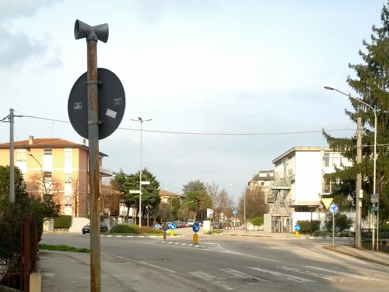 In this picture we can see a 4 way street surrounded with houses, trees and poles.