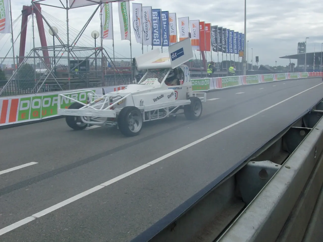 There is a white color vehicle on the road and there are few flags which has something written on...