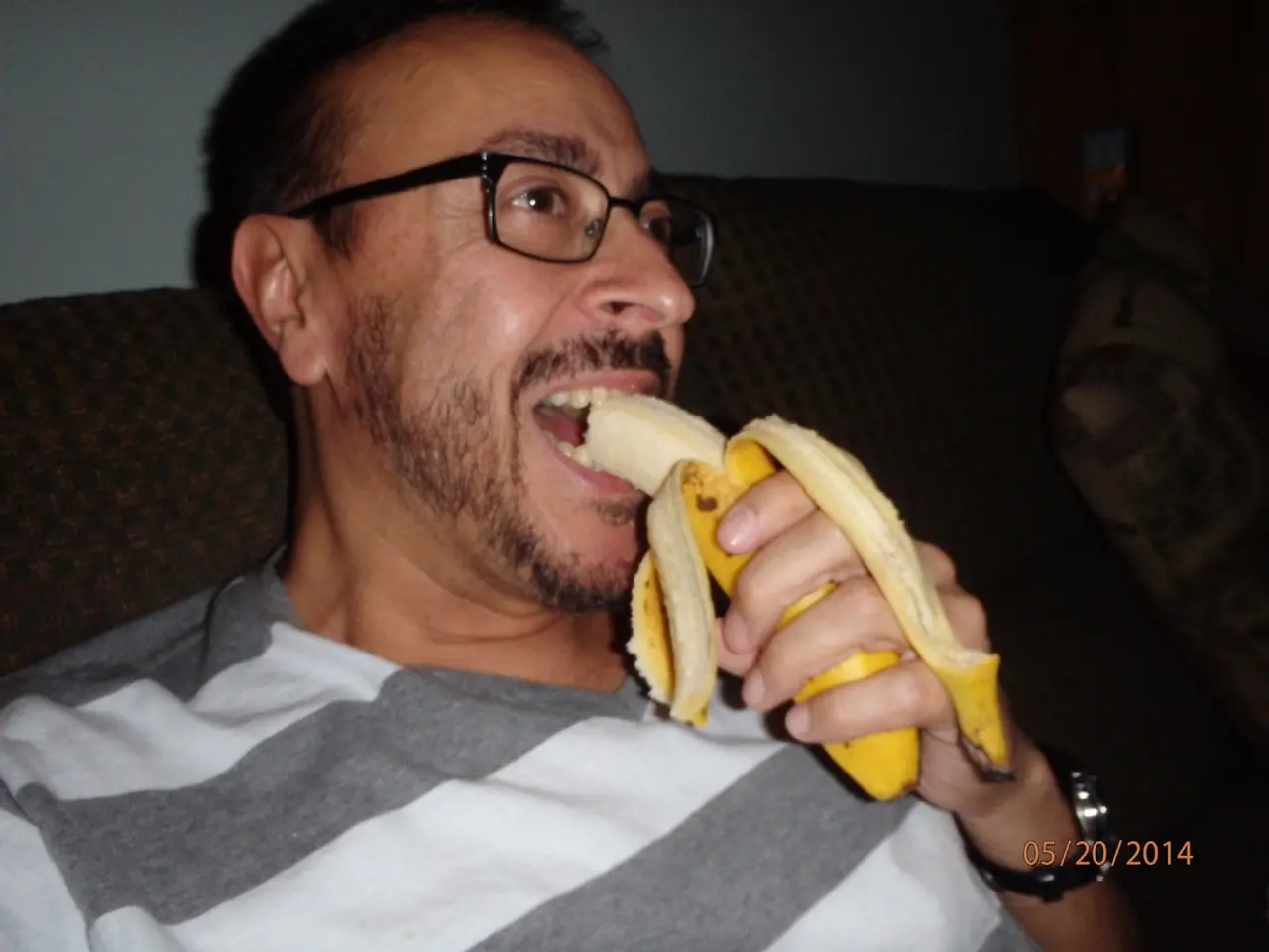 In this image, there is a man sitting and he is eating a banana, at the right side there is a...