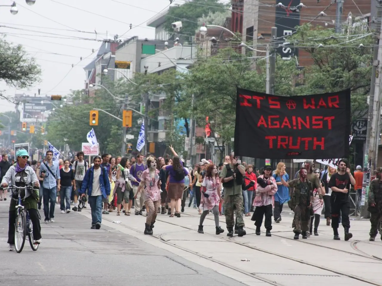 In this image there are a few people holding flags, banners are marching down the road and there is...