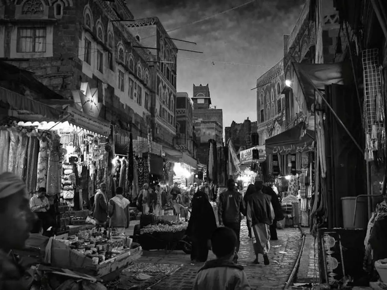 This is a black and white image. I can see groups of people walking. I can see few people standing....