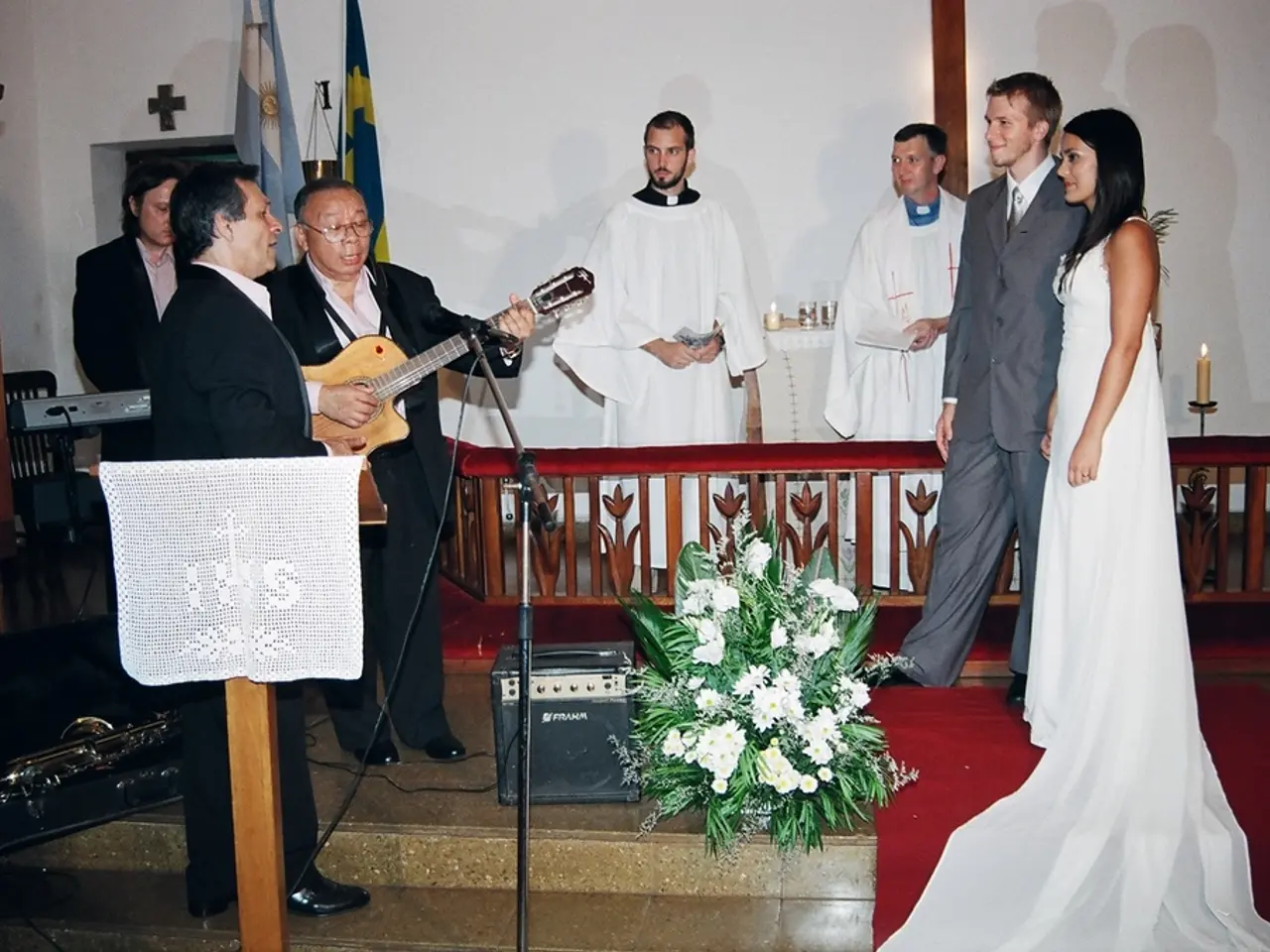 This picture is taken inside a room. It seems to be wedding. There are two pastors, bride,...