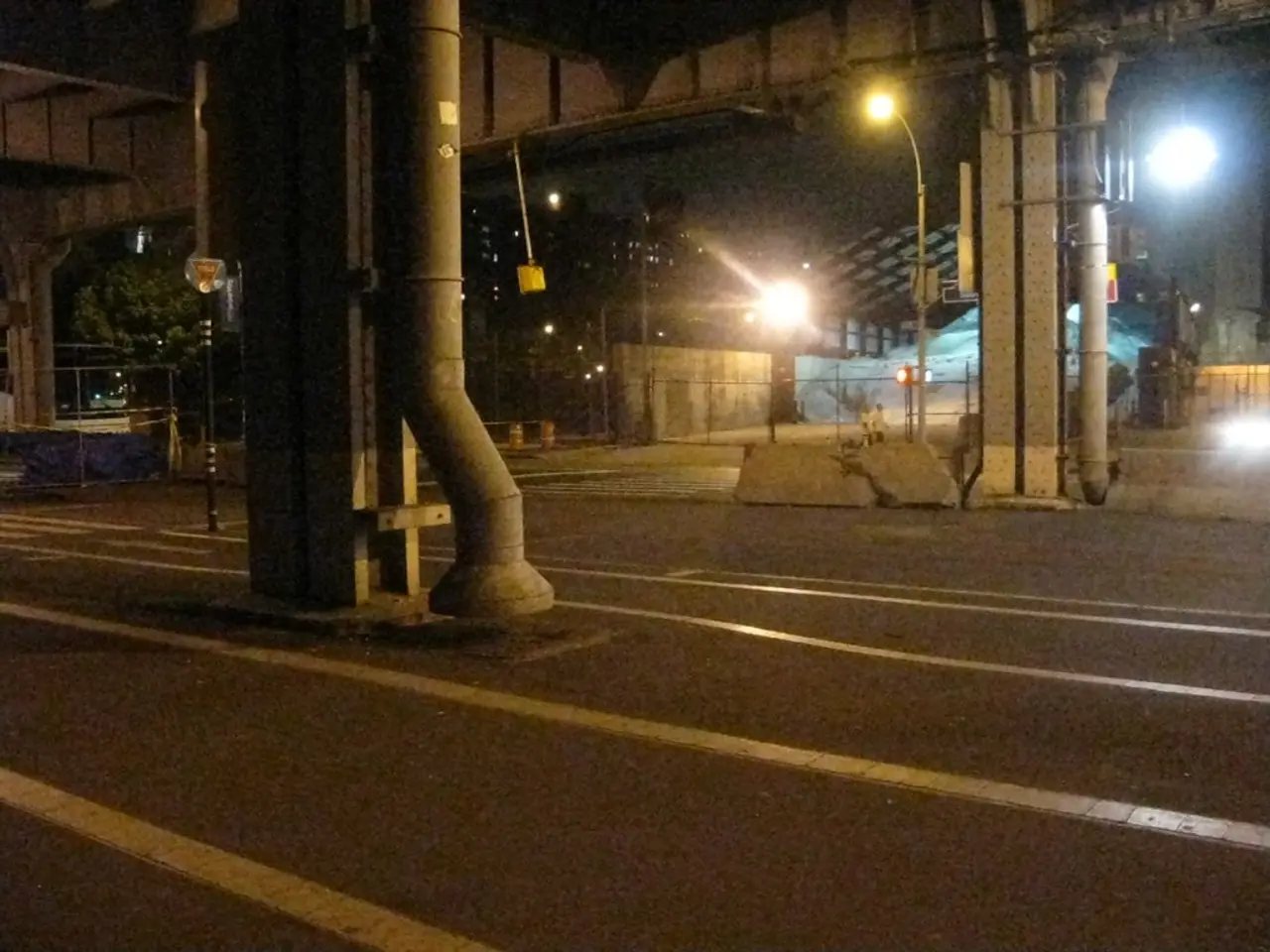 In the foreground of this image, there is a road, pillars, pipes, poles,lights, a shed, fencing,...