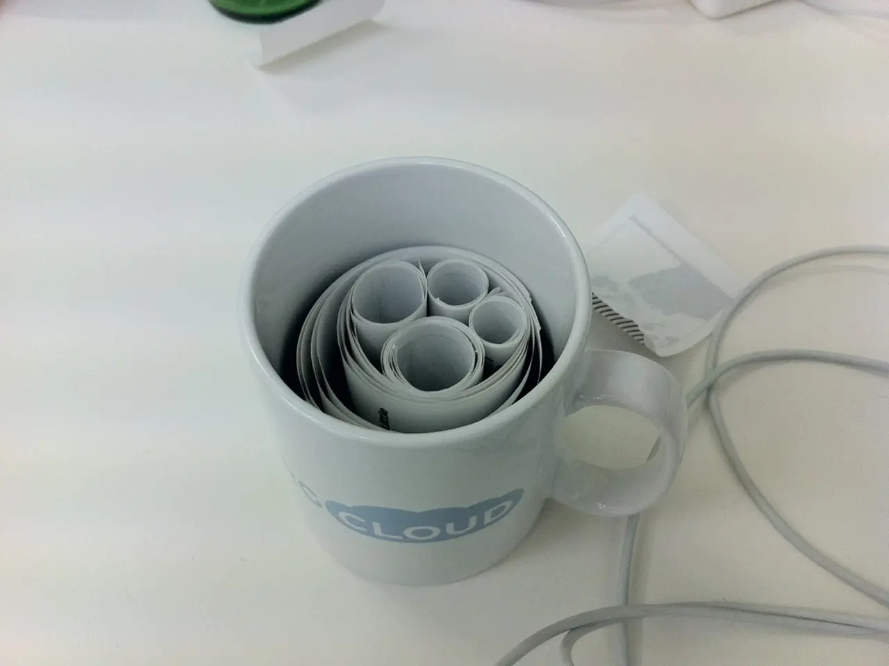 In the image there is a coffee cup with paper roll inside it on a table, beside it there is a wire...