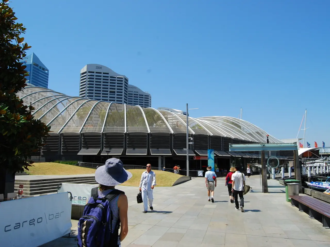 In this image there are a few people walking on the pavement, on the right side of the image there...