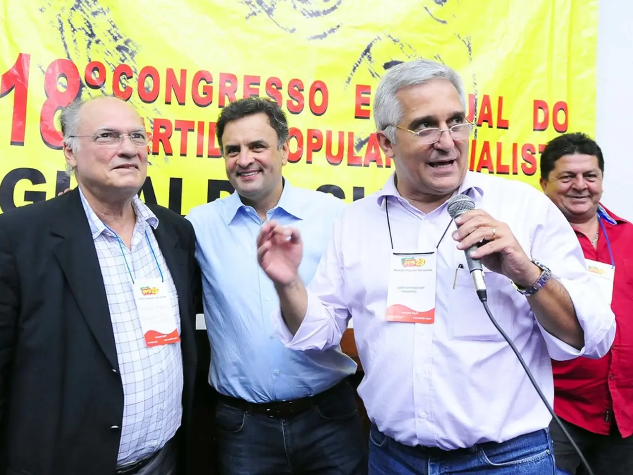 In the picture we can see some men are standing and one man is talking into the microphone and...