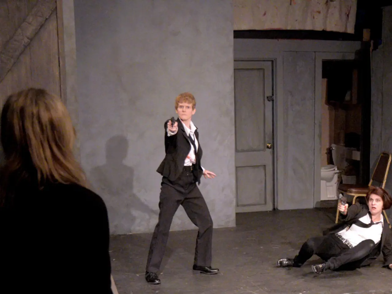 This picture shows an interview of a room. We see a woman seated on the ground and holding a gun in...