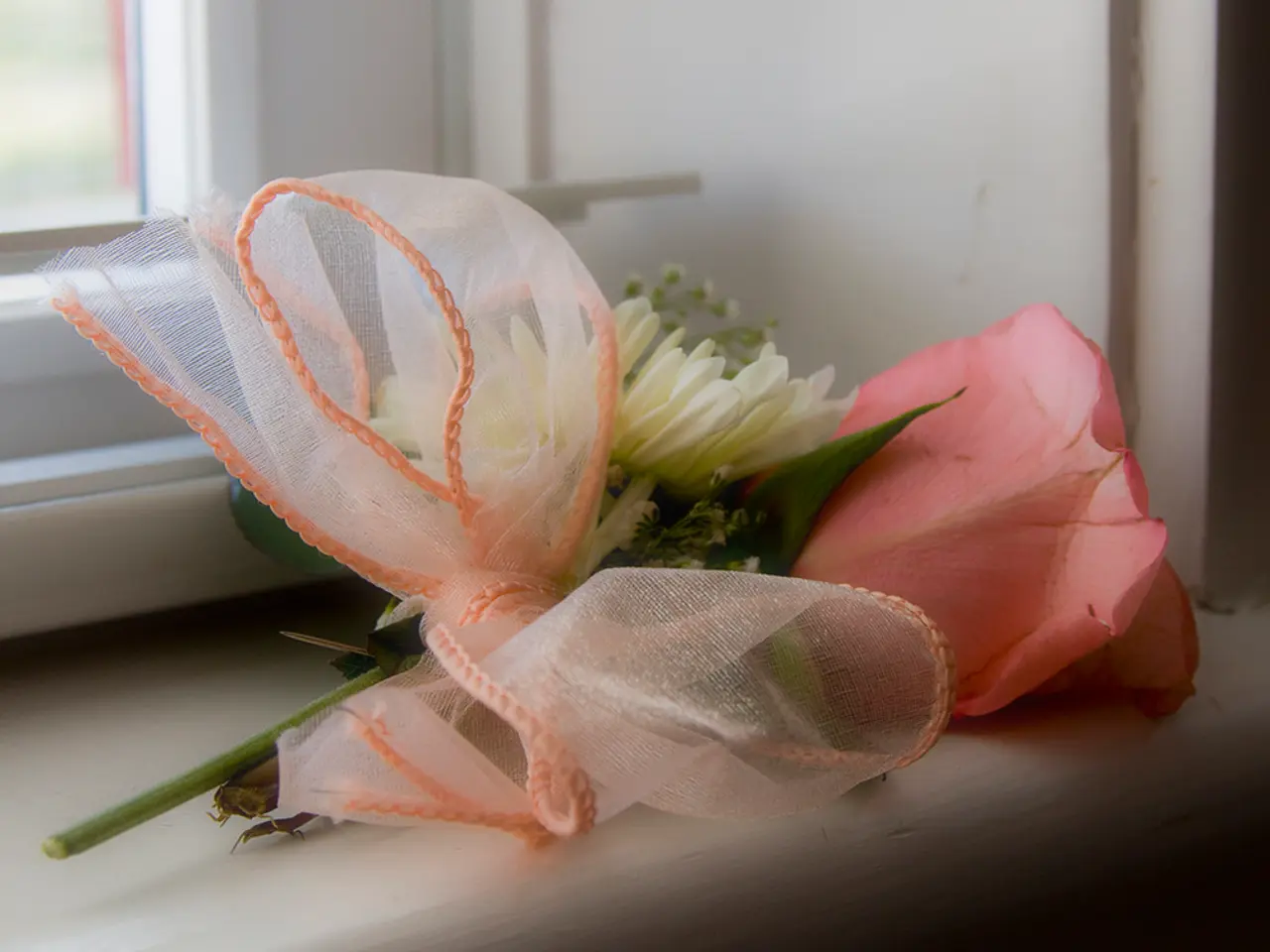 In this image there are flowers tied with a ribbon, and in the background there is a window.