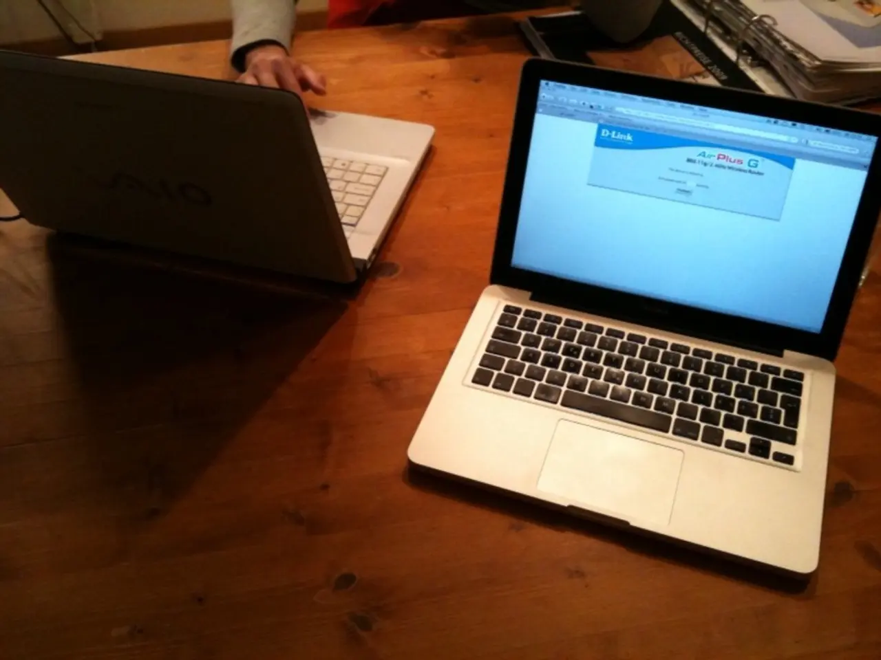 In this image there are two laptops kept on the wooden table. In the background there is a bunch of...