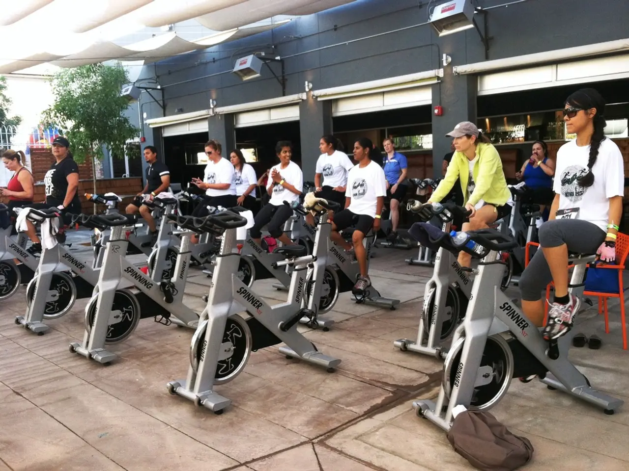 In this image I can see there are exercise cycles. Few people are doing workout on them, they wore...