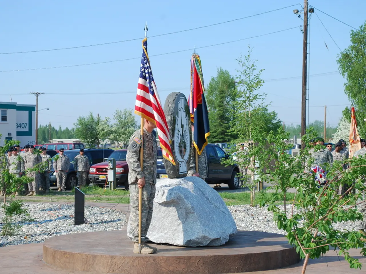 In front of the image there are two army personnel standing by holding flags, in between them there...