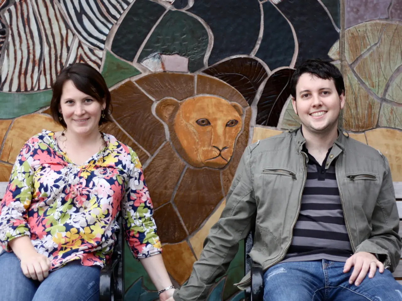 This picture is clicked outside. In the foreground we can see a man wearing blazer, smiling and...